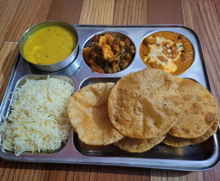 Hostel meal thali with rice, poori, dal, paneer curry and vegetable side dish