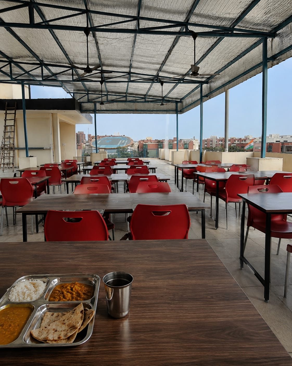 Rooftop open-air mess and dining area with seating, fans and city view